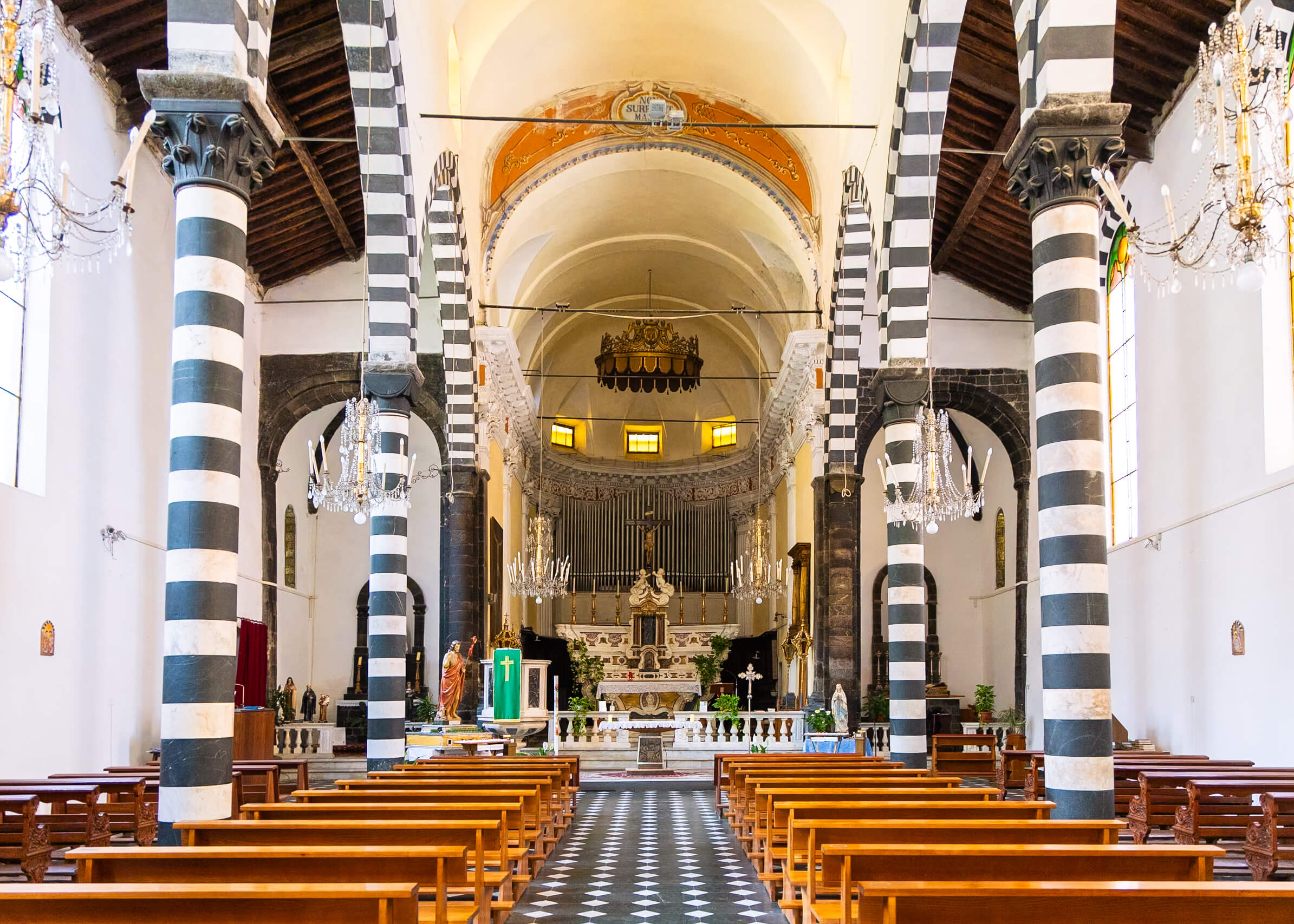 Interior view of the Church of San Giovanni Battista in Monterosso al Mare, Cinque Terre. The church features distinctive black and white striped columns, elegant chandeliers, and a beautifully decorated altar. This architectural gem is a highlight on any Cinque Terre itinerary.