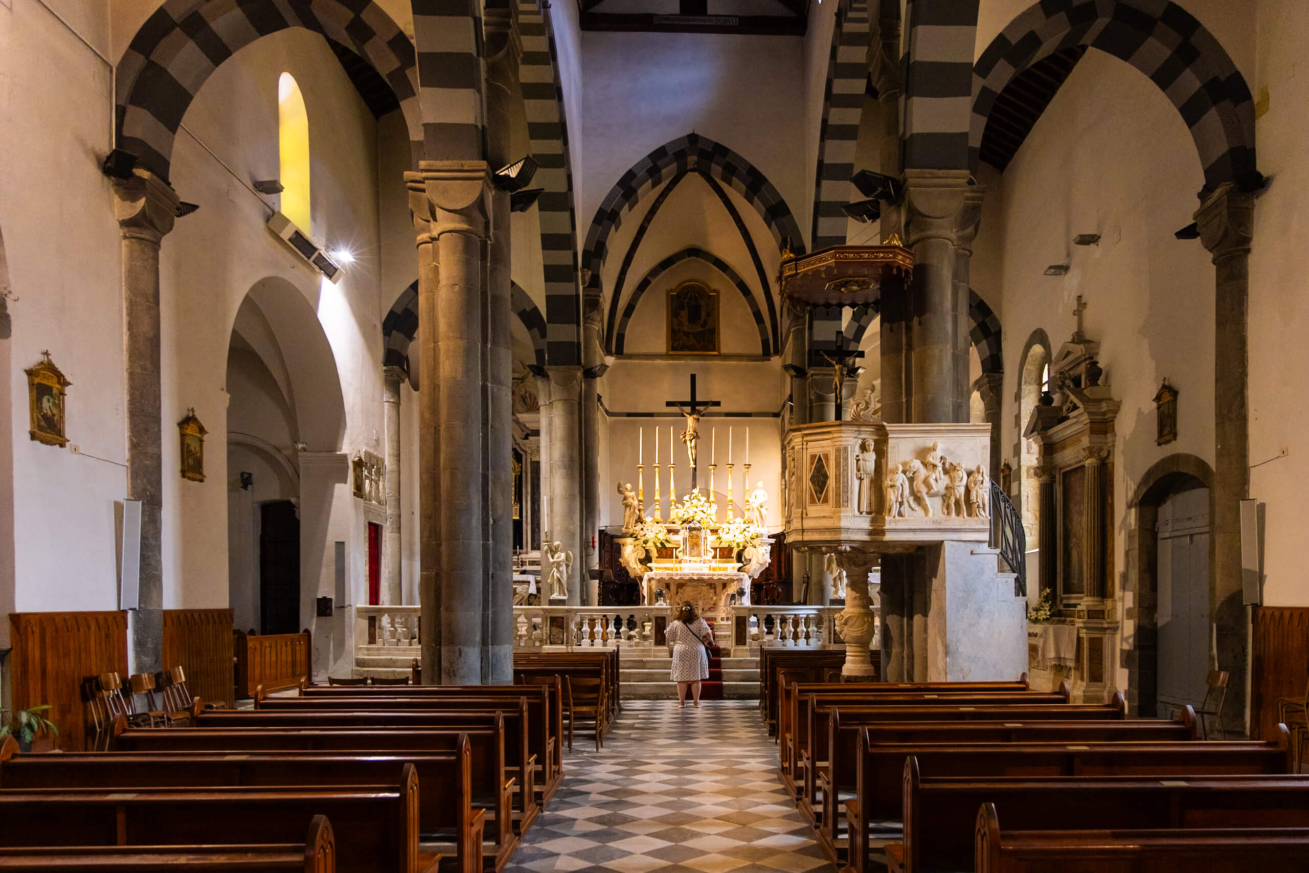 The interior of a church in Riomaggiore, showcasing its stunning architecture with striped columns and an elaborate altar. The setting exudes a serene and spiritual atmosphere.