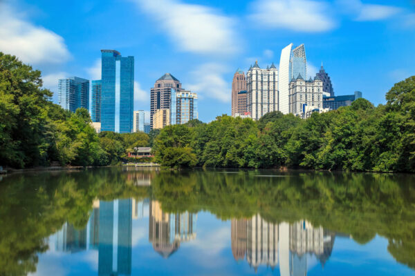 A serene view of Atlanta’s skyline reflecting on a still lake, framed by lush greenery on a bright summer day. Visiting this scenic spot in Piedmont Park is one of the most relaxing things to do in Atlanta, Georgia.