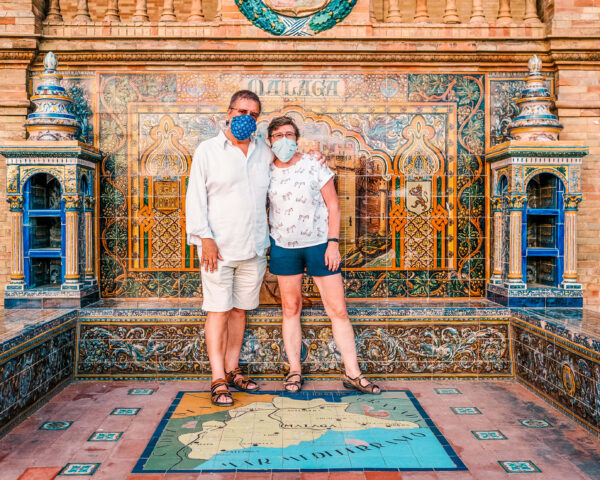 Penelope's parents stand in front of the colorful tiled Alicante alcove at Plaza de España. The tile map on the floor reads "Málaga" and "Mar Mediterraneo."